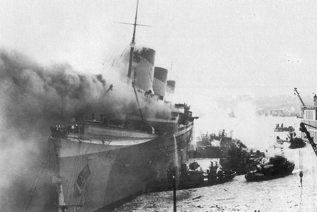 Février 1942, le Normandie (USS Lafayette) en feu dans le port de New York | Par US National Archives photo — http://www.navsource.org/archives/09/22/22053.htm, Domaine public